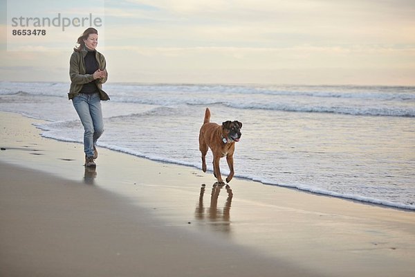 Reife Frau Spaziergang Hund am luftigen Strand