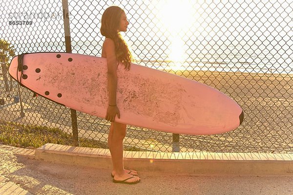 Mädchen am Strand stehend mit rosa Surfbrett