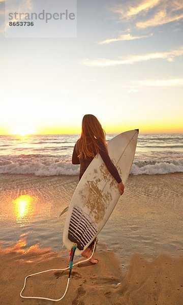 Mädchen am Strand mit Surfbrett im Neoprenanzug