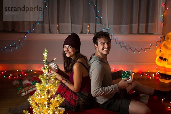 Junges Paar tauscht Geschenke im Wohnzimmer zu Weihnachten aus