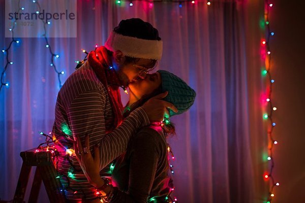 Ein junges Paar  das sich zu Weihnachten in Feenlicht gehüllt küsst.