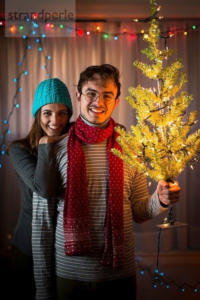 Junges Paar hält beleuchteten Weihnachtsbaum hoch