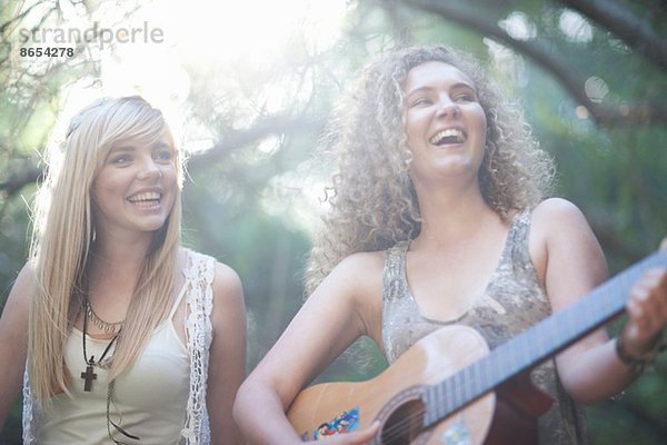 Zwei Teenager-Mädchen beim Gitarrespielen im Wald