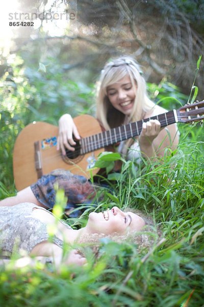 Zwei Teenager-Mädchen hören Gitarre im Wald