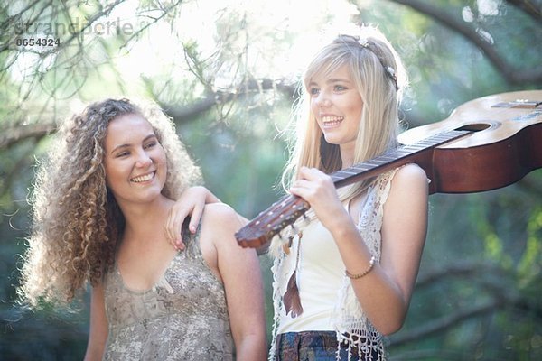 Zwei Teenagermädchen mit Akustikgitarre im Wald
