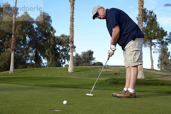 Porträt eines reifen männlichen Golfers  der auf Grün schießt