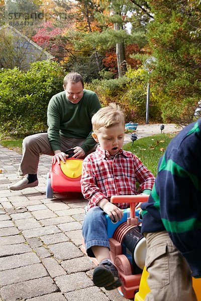 Vater und kleine Söhne beim Spielen auf Spielzeugautos im Garten