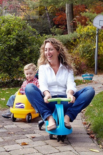 Mutter und Sohn fahren auf Spielzeugautos im Garten