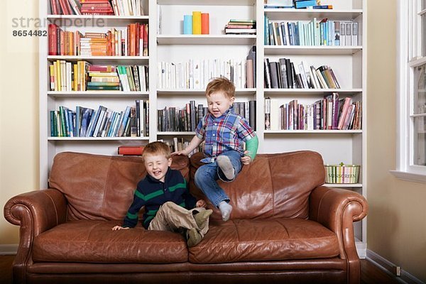 Zwei junge Brüder springen auf dem Sofa.