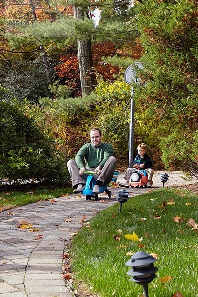 Vater und Sohn fahren auf Spielzeugautos im Garten