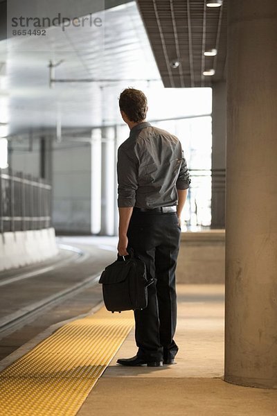 Mittlerer erwachsener Büroangestellter  der am Bahnhof auf den Zug aufpasst.