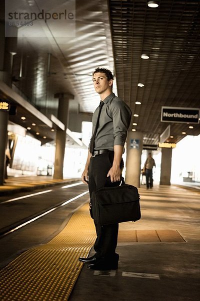 Mittlerer Erwachsener Geschäftsmann  der am Bahnhof auf den Zug wartet.