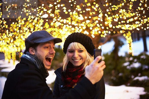 Junges Paar beim Selbstporträt mit Weihnachtsbeleuchtung im Freien