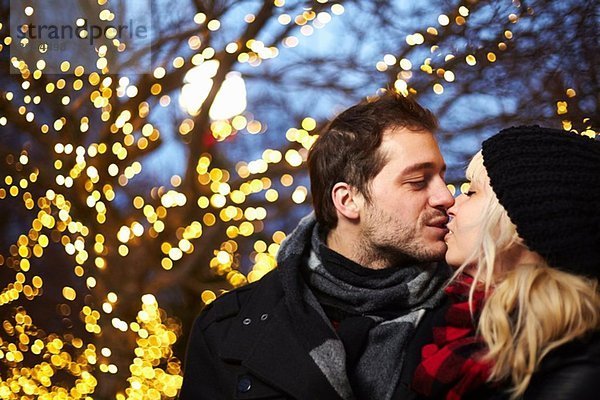 Junges Paar küsst sich vor den Weihnachtslichtern im Freien