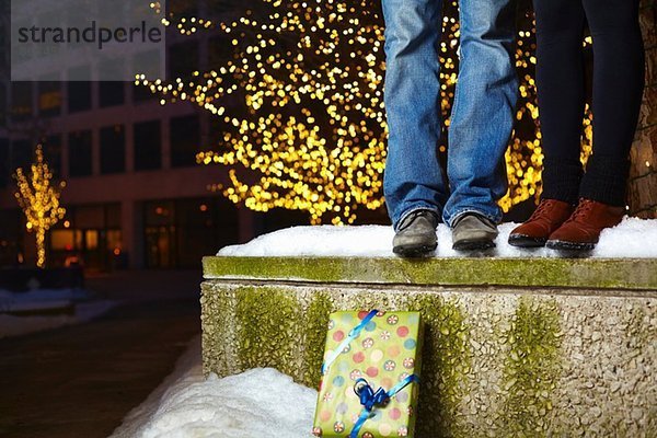 Die Beine eines jungen Paares  das auf einer schneebedeckten Mauer in der Stadt steht.