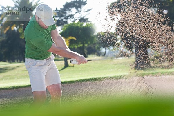 Junger Golfer  der aus dem Bunker spielt.