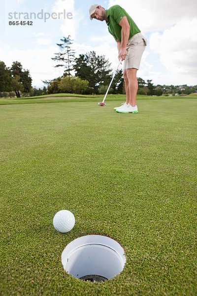 Junge männliche Golfspieler spielen den Ball auf dem Grün