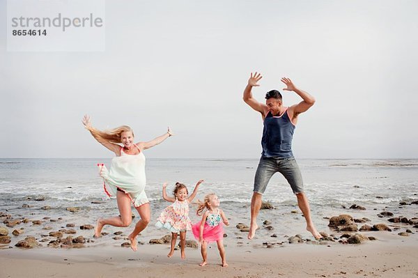 Eltern und zwei junge Mädchen beim Springen am Strand