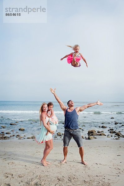 Eltern und zwei junge Mädchen  die am Strand herumalbern.