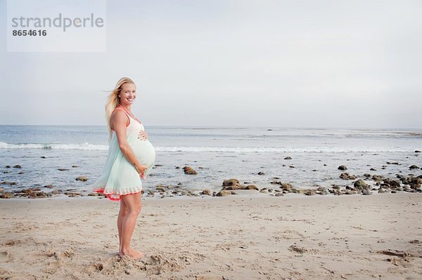 Porträt einer schwangeren jungen Frau am Strand