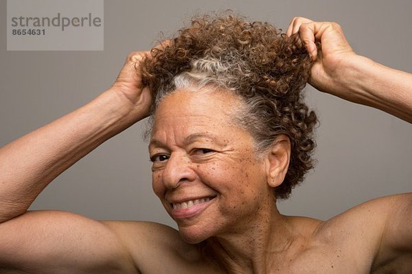 Nahaufnahme des Studioportraits einer älteren Frau beim Haareziehen
