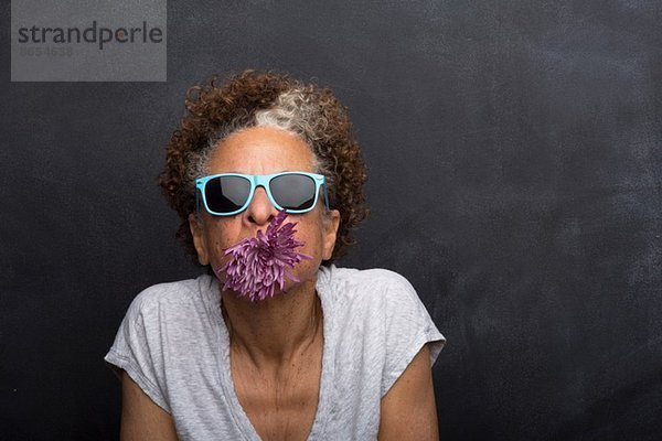 Studio-Porträt einer älteren Frau mit Blume im Mund