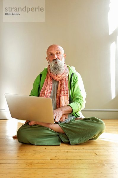 Senior Mann mit Laptop in Lotusstellung