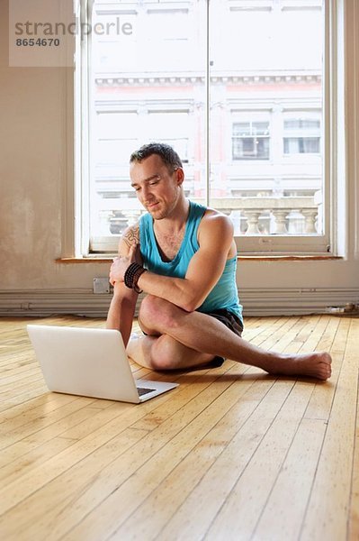 Mid Erwachsene Mann mit Laptop  während in Cowface Yoga-Pose