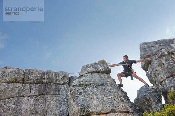 Junger Mann beim Treten und Greifen auf den Felsen