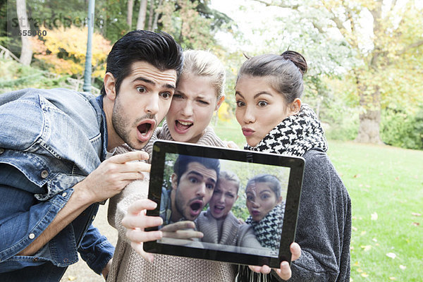 Freunde fotografieren sich selbst und machen lustige Gesichter mit einem digitalen Tablett im Freien.