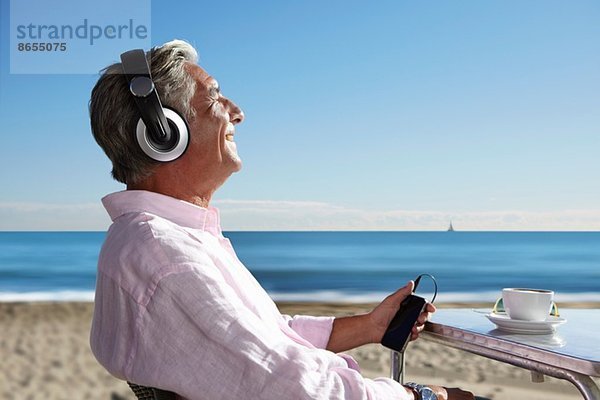 Senior Mann hört Musik mit Kopfhörern am Strand