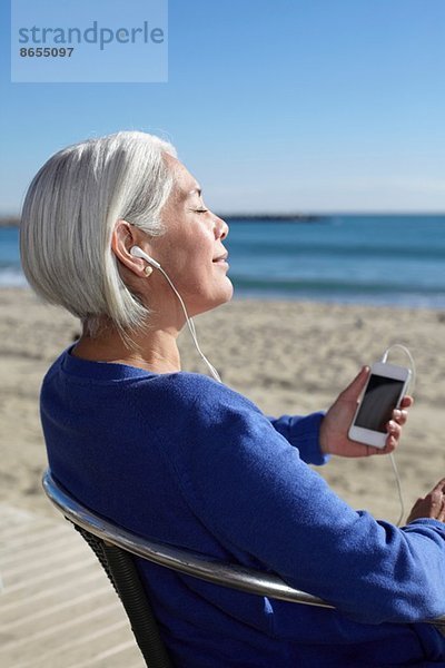 Reife Frau beim Musikhören mit Ohrstöpseln am Strand