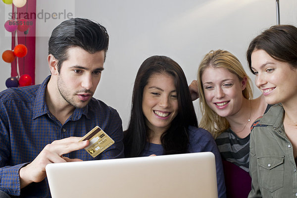 Freunde versammelt um Laptop-Computer Vorbereitung auf die Verwendung von Kreditkarte für den Online-Einkauf