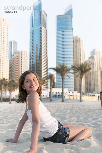 Mädchen am Strand sitzend  über die Schulter lächelnd