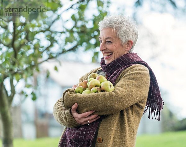 Fröhliche Seniorin mit einem Arm voller Äpfel