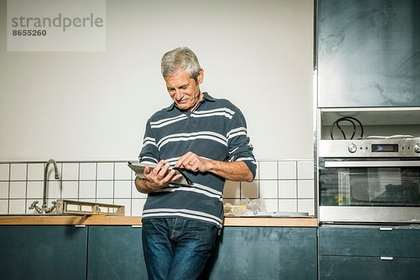 Senior Mann mit digitalem Tablett in der Küche