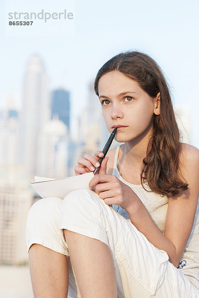 Preteen Mädchen sitzen im Freien mit Stift und Papier  Blick nach oben in Gedanken
