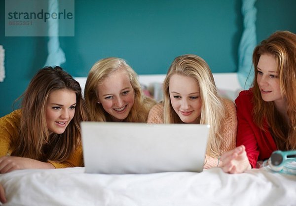 Vier Mädchen im Teenageralter betrachten Laptop im Schlafzimmer