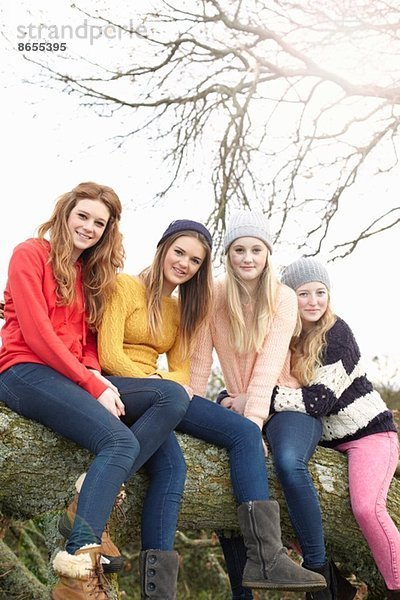 Vier Teenager-Mädchen auf Baumstamm sitzend