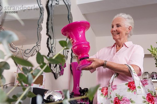 Seniorin hält Vase im Blumengeschäft hoch
