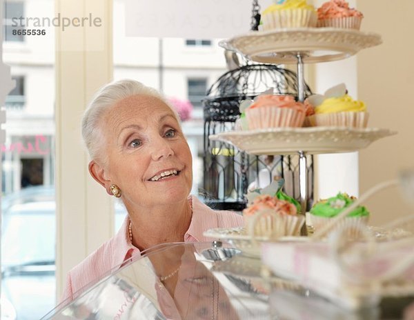 Seniorenfrau beim Betrachten von Muffins im Café