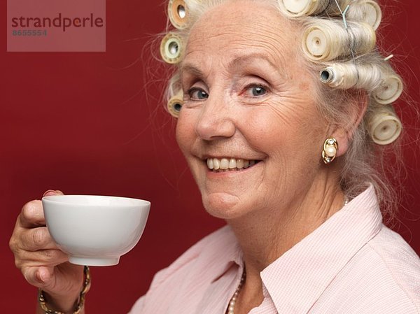Studio-Porträt der älteren Frau in Haarrollen mit Tasse Tee