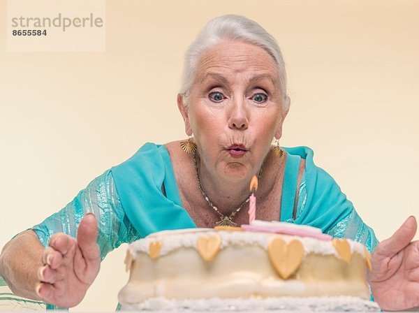 Studio-Porträt der Seniorin beim Ausblasen der Geburtstagskerze