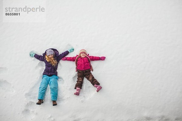 Zwei Schwestern spielen und machen Schnee-Engel im Schnee