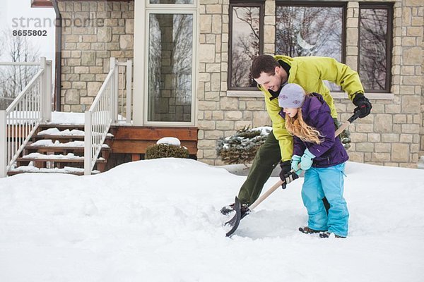 Vater hilft Tochter beim Schneeschaufeln
