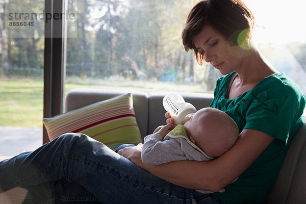 Mutter Fütterungsflasche für den Jungen auf dem Sofa