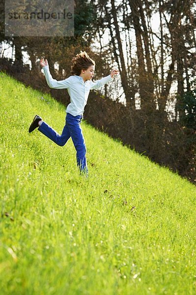 Kleiner Junge rennt steiles Grasfeld hinunter