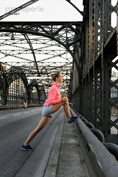 Junge Läuferin streckt Beine auf Brücke