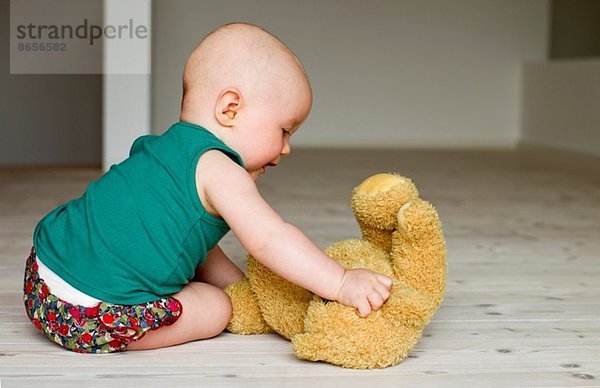 Kleines Mädchen spielt mit Teddybär auf dem Boden