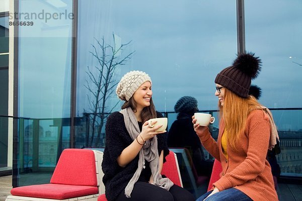 Zwei junge erwachsene Frauen genießen Kaffee auf der Dachterrasse